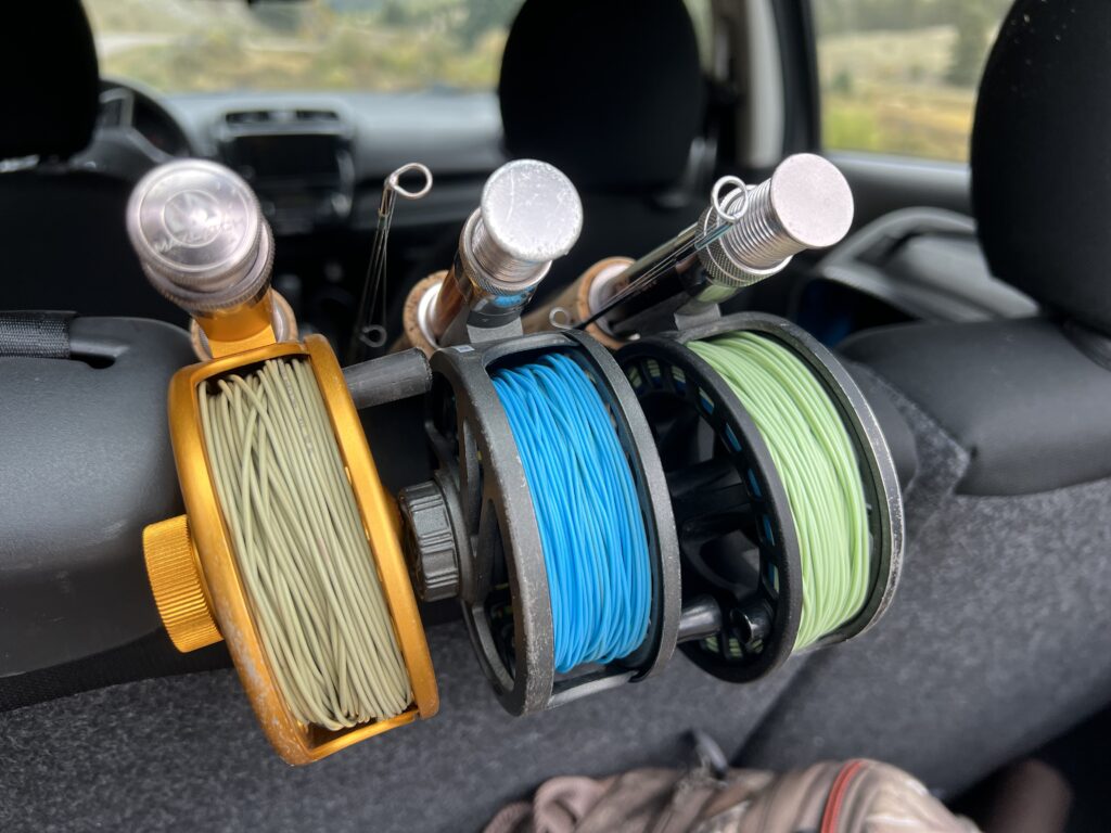 3 fly rod butts with fly fishinf reels attached all dofferent colors.